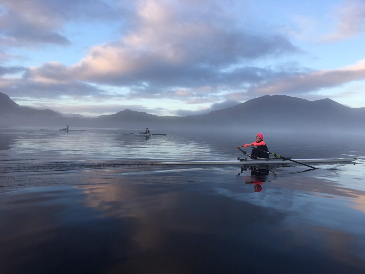 Single sculler at dawn with mist over the lake and mountains